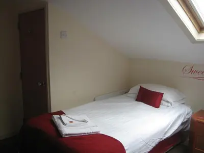 a small bedroom with a white bed with a red pillow at The Dragonfly in Blackpool