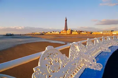 a white bench on the beach with a lighthouse at The Galloway in Blackpool