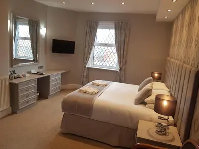 a bedroom with a bed and a desk and two windows at Bedford Hotel in Lytham St Annes
