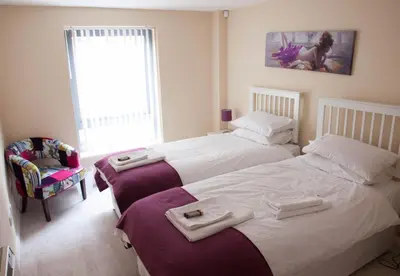 a bedroom with two beds and a chair and a window at City Centre Luxury Holiday Apartment in Liverpool