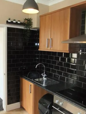 a kitchen with a sink and a black tiled wall at Dewsbury House in Blackpool