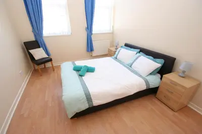 a bedroom with a large bed with blue curtains at MARLEY MANSIONs APARTMENTS - KING ST REF : 10/3 in Wallasey