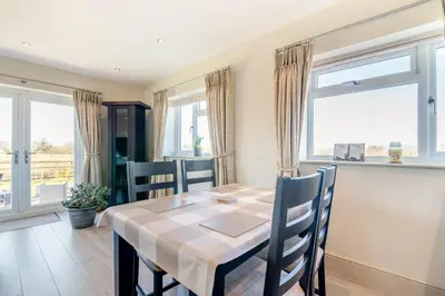 a dining room with a table and chairs and windows at Palms Cottage in Blackburn
