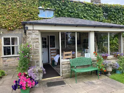 a green bench sitting outside of a house with flowers at Chapel Cottage Clitheroe Road in Waddington