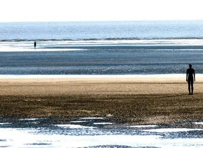 a man standing on a beach with a surfboard at Beach house in Crosby