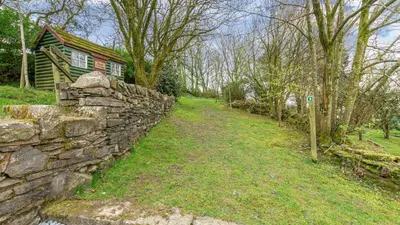 a stone wall next to a house and a building at Hill Side Barn in Ireleth