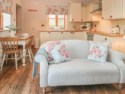 a living room with a blue couch and a kitchen at Maltkiln Cottage At Crook Hall Farm in Mawdesley