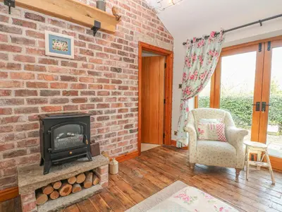 a living room with a brick fireplace and a chair at Maltkiln Cottage At Crook Hall Farm in Mawdesley