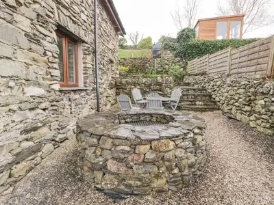 a patio with two chairs and a stone wall at Eller Riggs Cottage in Ulverston