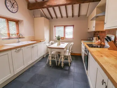 a kitchen with a table and a clock on the wall at Barn Owl Cottage At Crook Hall Farm in Mawdesley