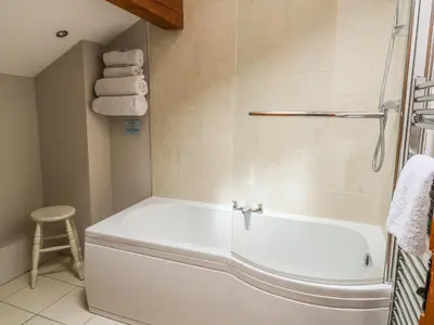 a white bath tub in a bathroom with a stool at Barn Owl Cottage At Crook Hall Farm in Mawdesley