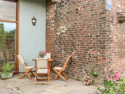 a patio with chairs and a table and a brick wall at Barn Owl Cottage At Crook Hall Farm in Mawdesley