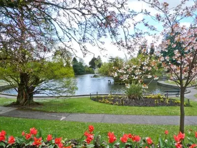 a park with a lake with a tree and flowers at Baytree Apartment in Grange Over Sands
