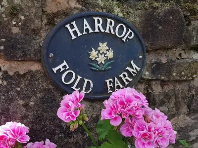 a sign on a stone wall with pink flowers at Stone Mouse Cottage in Harrop Fold