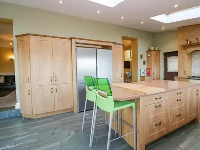 a kitchen with wooden cabinets and green bar stools at Groffa Crag Farmhouse in Lowick Green