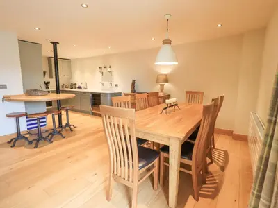 a dining room and kitchen with a wooden table and chairs at Yew Cottage in Backbarrow
