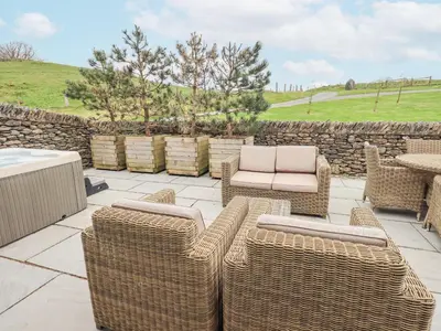 a patio with wicker furniture and a stone wall at Lime Cottage in Backbarrow
