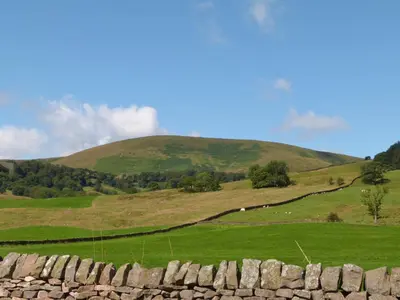 a field with a hill in the background with a stone wall at Saetr Cottage in Harrop Fold