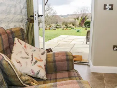 a living room with two chairs and a sliding glass door at Saetr Cottage in Harrop Fold
