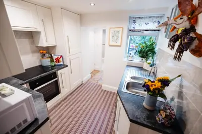 a kitchen with white cabinets and a sink with flowers on the counter at Oh So Snug in Whalley