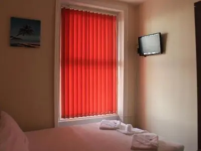 a bedroom with a window with red curtains and a television at The Royal Windsor Hotel in Blackpool