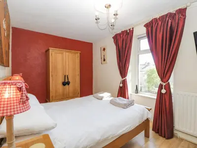 a bedroom with a bed and a window with red curtains at Beech Cottage in Ulverston
