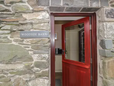 a red door in a stone building with a sign at Woodside Barn in Ulverston