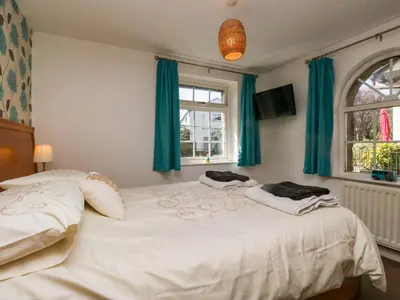 two beds in a bedroom with green curtains and a tv at The Old Mill in Grange Over Sands