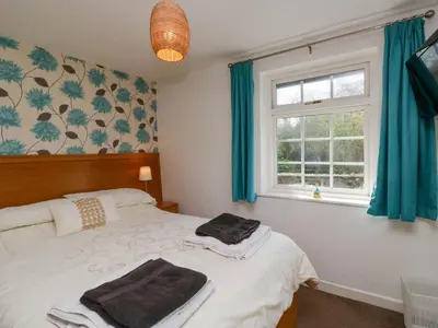 a bedroom with a bed with blue curtains and a window at The Old Mill in Grange Over Sands