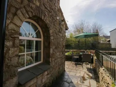 a stone building with a window and a table with an umbrella at The Old Mill in Grange Over Sands