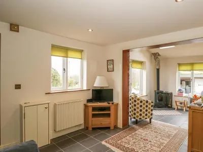 a living room with a tv and a desk and windows at Beck Cottage in Ulverston