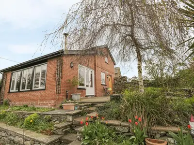 a brick house with a tree and some flowers at Beck Cottage in Ulverston
