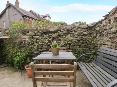 a table and a bench in front of a stone wall at Mulberry Cottage in Grange Over Sands