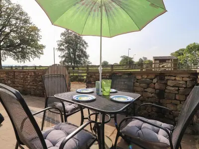 a table with a green umbrella on a patio at Stable Cottage in Burton in Lonsdale