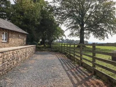 a fence next to a stone wall next to a field at Stable Cottage in Burton in Lonsdale
