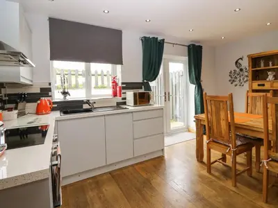 a kitchen with white cabinets and a table and a dining room at Bluebell Cottage in Ulverston