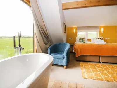 a bathroom with a tub and a bedroom with a bed and a chair at Bluebell Cottage in Ulverston