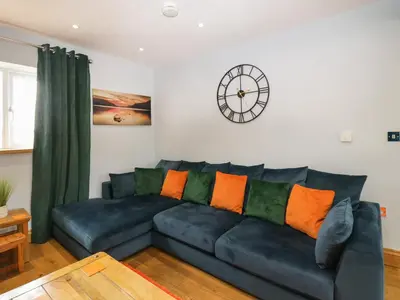 a living room with a blue couch and a clock on the wall at Bluebell Cottage in Ulverston