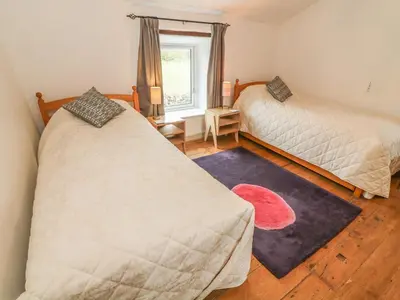 a bedroom with two beds and a red rug at Rosemary Cottage in Carnforth