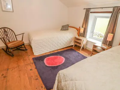 a bedroom with two beds and a chair and a window at Rosemary Cottage in Carnforth