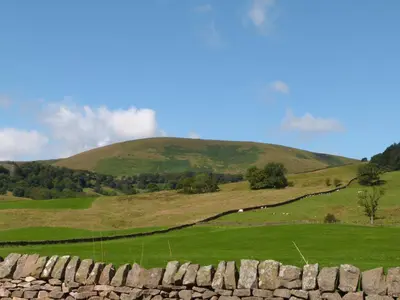 a green field with a stone wall and a hill at The Old Post Office in Garstang