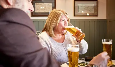 a woman drinking a glass of beer in a pub at The Bluebird Inn at Samlesbury in Preston