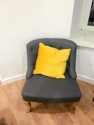 a yellow pillow sitting on a grey chair at Garden Apartment in Grange Over Sands