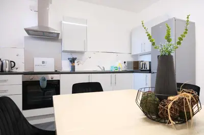 a white kitchen with a table and a vase with a plant at The Docklands Apartment by Serviced Living Liverpool in Liverpool