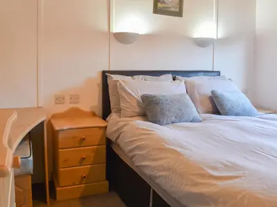 a bed with white sheets and pillows next to a night stand at Tranquillity in Millom