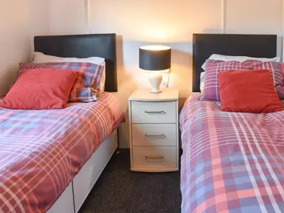 a bedroom with two beds and a lamp on a night stand at Tranquillity in Millom