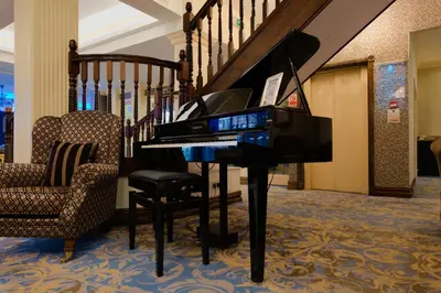 a piano in a living room with a chair and stairs at Clifton Park Hotel - Adults Only in Lytham St Annes