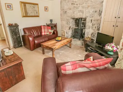 a living room with leather furniture and a stone fireplace at Herdwick Cottage in Grange Over Sands