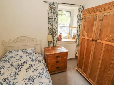 a bedroom with a bed and a dresser and a window at Herdwick Cottage in Grange Over Sands