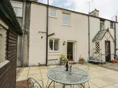a patio with a glass table in front of a building at Herdwick Cottage in Grange Over Sands
